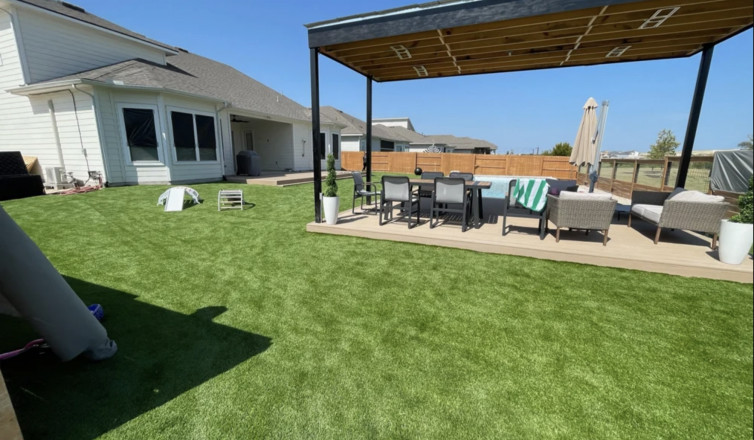 A wide shot of a backyard with artificial turf installed around a pergola with seating in the middle.